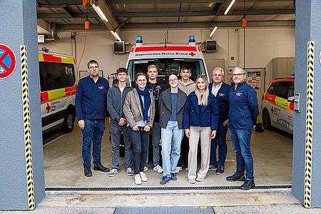 In der Fahrzeughalle des Rettungsdienstes stehen die 6 der 7 Freiwilligen vor einem Krankentransportwagen. Neben Ihnen stehen links der Katastrophenschutzbeauftragte Matthias Macht und rechts der Leiter des Rettungsdienstes Johann Haider und sein Stellvertreter Franz Bauer. Auf dem Bild sind 3 männliche und 3 weibliche Bundesfreiwillige.